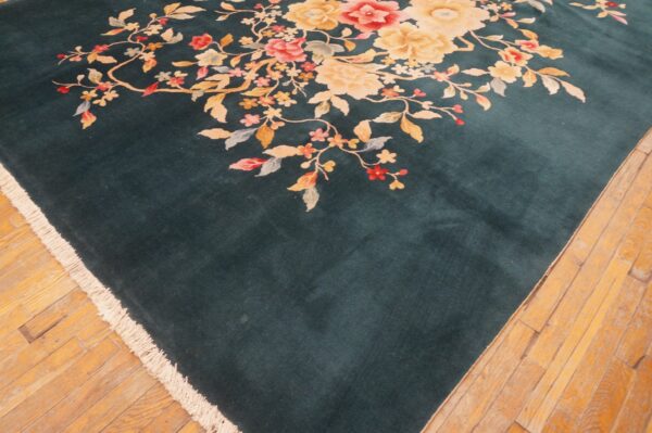 A velvety teal rug featuring large pink and yellow floral sprays is displayed on light plank wood flooring.