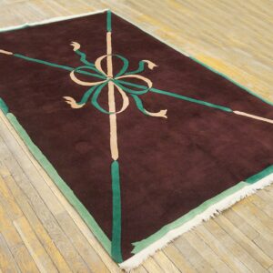 Brown rug with a geometric green and tan bow pattern on distressed light wood plank flooring.