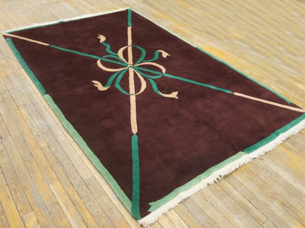 Brown rug with a geometric green and tan bow pattern on distressed light wood plank flooring.