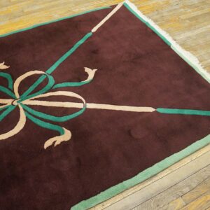 Maroon rug with a geometric beige and teal ribbon design on worn diagonal wood plank flooring.