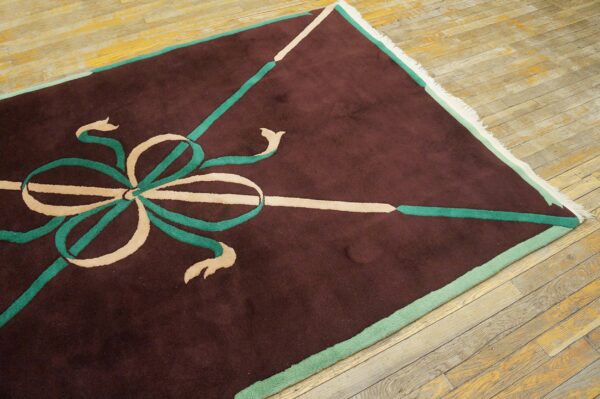 Maroon rug with a geometric beige and teal ribbon design on worn diagonal wood plank flooring.