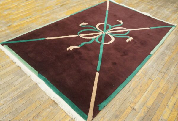 Maroon rug with a high pile and a central teal and cream ribbon motif on wood flooring.
