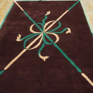 Dark brown rug with a stylized teal and beige ribbon design, laid over worn wood flooring.