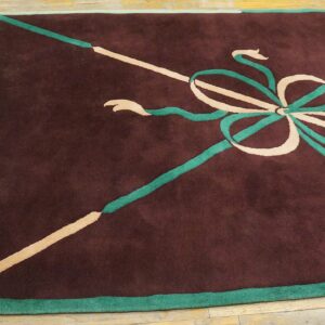 Maroon rug featuring a stylized tan and teal bow pattern and white fringe on worn wood flooring.