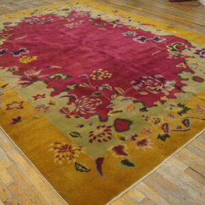 Large magenta rug with mustard yellow and pale green floral borders on worn wooden floorboards.
