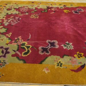 Ornate floral rug with a deep red field and complex green and mustard borders on a light wood floor.