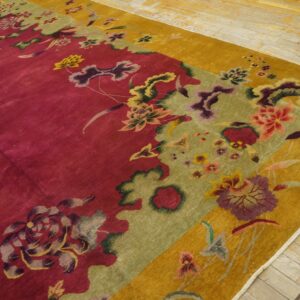 Deep magenta rug with gold and green borders featuring large stylized floral patterns on light wood floor.