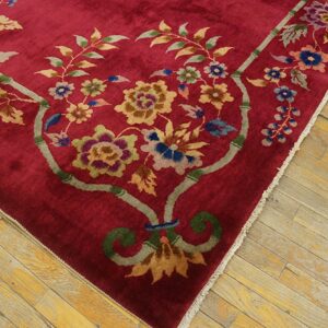 Plush crimson rug featuring a colorful bamboo and floral design rests on worn wood flooring.