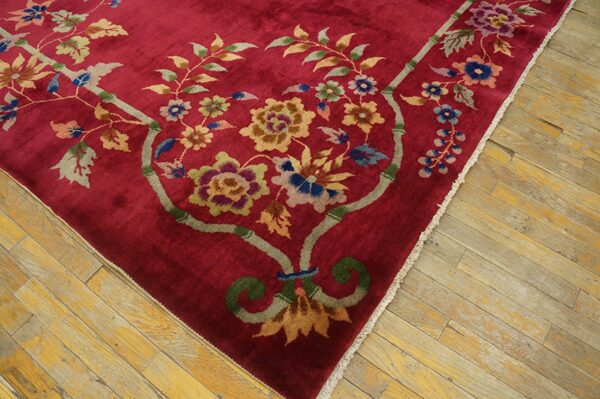 Plush crimson rug featuring a colorful bamboo and floral design rests on worn wood flooring.