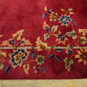 Crimson high-pile rug detail showing multicolored floral vines and a pale band bordering light wood flooring.