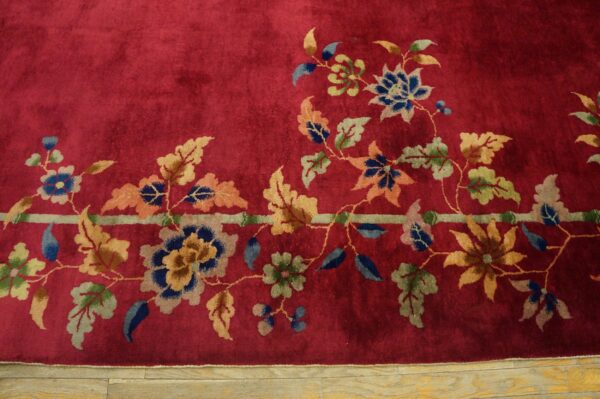 Crimson high-pile rug detail showing multicolored floral vines and a pale band bordering light wood flooring.