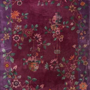 Plush velvety burgundy rug displays an ornate border of colorful flowers, vines, and two hanging vases.