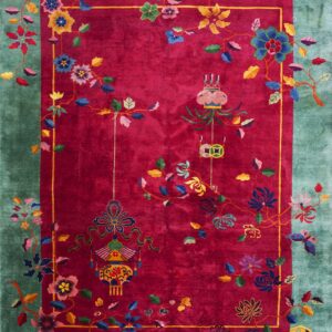 A velvety magenta rug featuring a colorful vine, flower, and lantern pattern within a teal border.