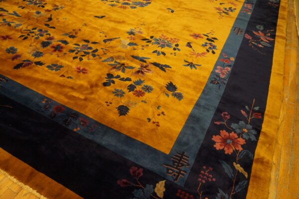 Gold rug with high pile and dark blue floral motifs, bordered by teal and navy on wood planks.