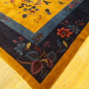 Deep pile yellow rug with blue and navy stepped borders, detailed florals, resting on wood planks.