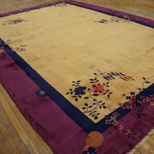 Low-pile tan rug with stylized blue and pink florals, bordered in navy and rich purple, on hardwood.