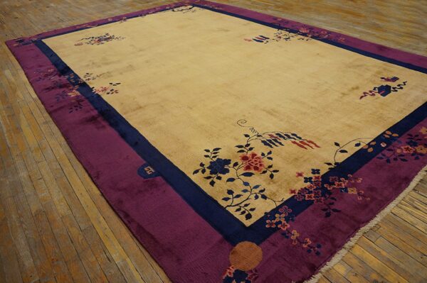 Low-pile tan rug with stylized blue and pink florals, bordered in navy and rich purple, on hardwood.