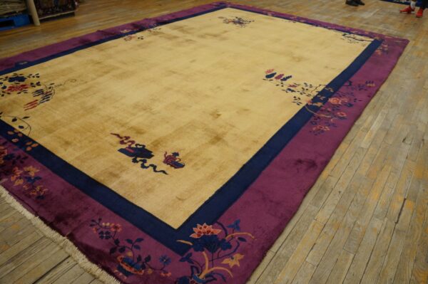 Gold rug with floral designs and purple border rests on worn wood plank flooring.