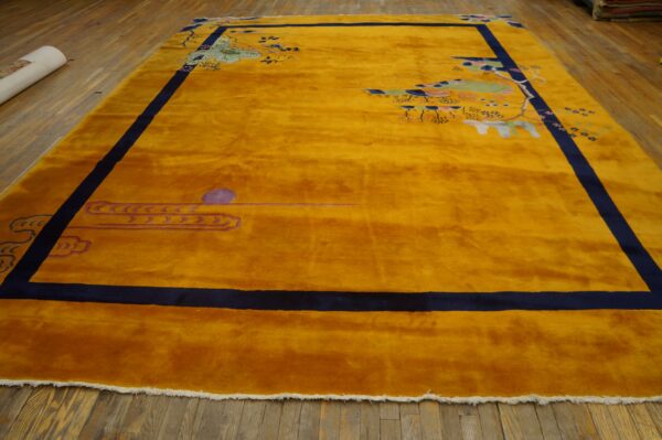 Plush gold rug with navy blue border and scattered asian motifs lays on rustic wood planks.