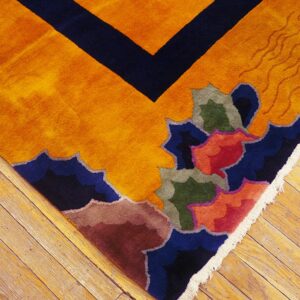 Detail shot of a bright orange rug with complex abstract designs and a navy geometric border on wood flooring.