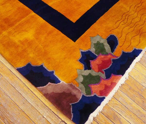 Detail shot of a bright orange rug with complex abstract designs and a navy geometric border on wood flooring.