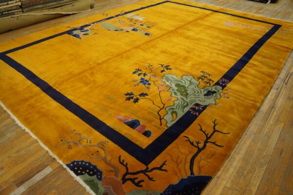 Shimmering gold rug with a navy border and detailed landscape pattern rests on distressed wood flooring.