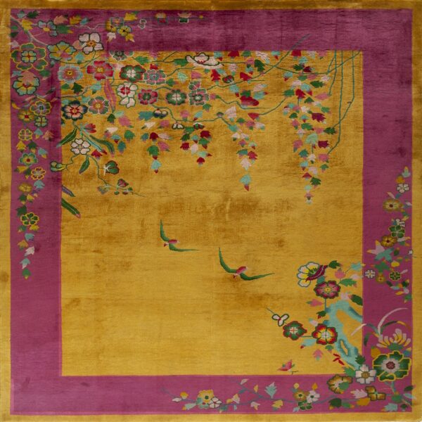 A low-pile gold rug with a magenta border featuring multicolored stylized floral and bird designs.