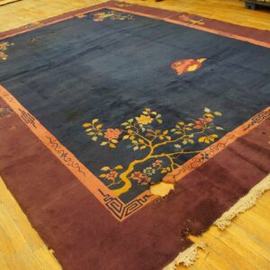 Dark blue rug with maroon and orange borders, showing floral patterns, rests on wooden floorboards.
