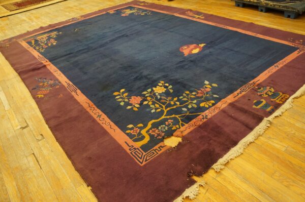 Dark blue rug with maroon and orange borders, showing floral patterns, rests on wooden floorboards.