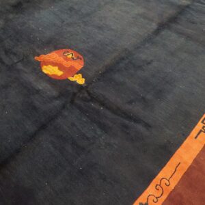 Dark blue rug field with red and yellow stylized motif next to an orange border stripe with fretwork.