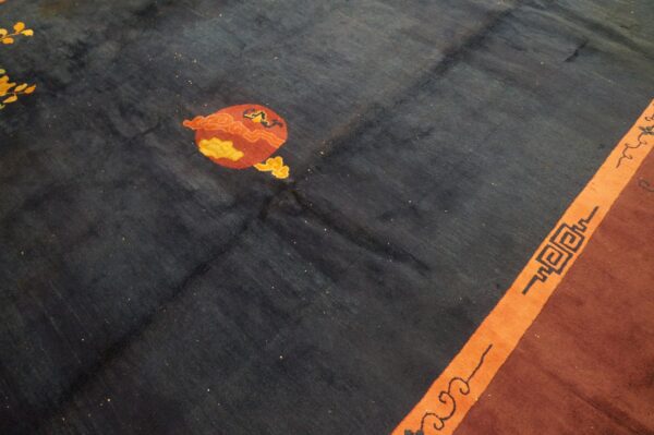 Dark blue rug field with red and yellow stylized motif next to an orange border stripe with fretwork.