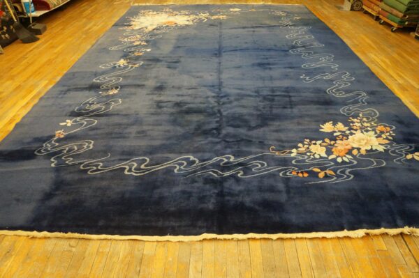 Deep blue high-pile rug featuring a border of white waves and pale orange floral patterns on wood planks.