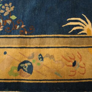 Blue rug detail featuring pink floral motifs, thin blue lines, and a wide golden border with abstract designs.