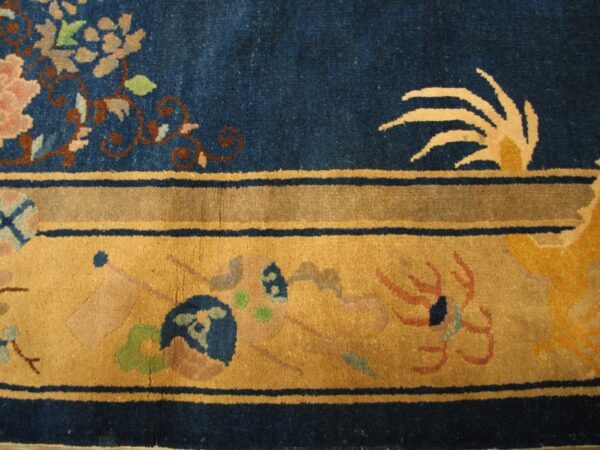 Blue rug detail featuring pink floral motifs, thin blue lines, and a wide golden border with abstract designs.