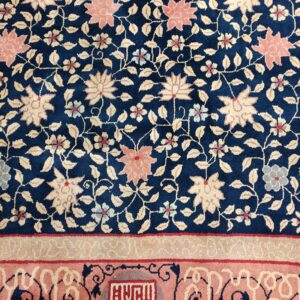 Dark blue rug with dense floral pattern and a dusty pink border featuring a symbolic cartouche.