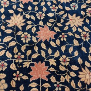 Deep blue plush rug with a dense floral pattern featuring coral blooms and tan leaves; a red border is visible.