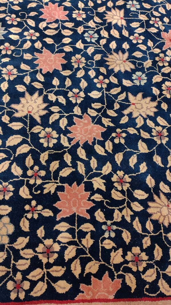 Deep blue plush rug with a dense floral pattern featuring coral blooms and tan leaves; a red border is visible.