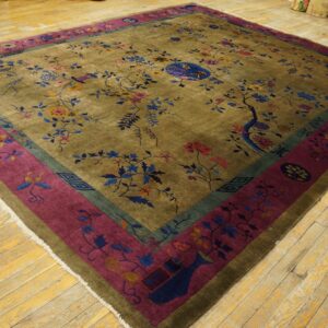 Multi-colored floral rug with an olive field and wide magenta border lying on light-toned wood flooring.