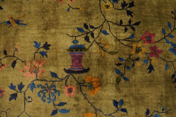 High-pile olive rug with a stylized vase, bird, and pink and blue flowering vine pattern.
