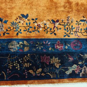 Close-up of a high-pile rug with golden orange and deep blue floral and bird patterns.