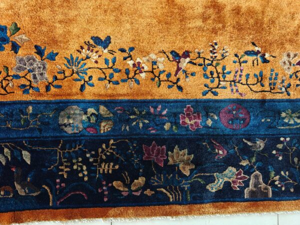 Close-up of a high-pile rug with golden orange and deep blue floral and bird patterns.