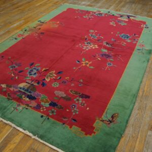 Red rug with green border and multicolor botanical motifs, including birds, sits on wood flooring.