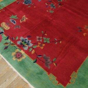 A vibrant red rug featuring scattered multicolor floral motifs and a wide teal green border on distressed hardwood floors.