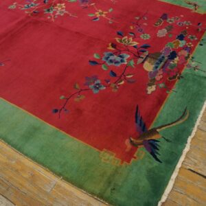 Vivid red rug with a wide green border, featuring detailed multicolored floral designs and exotic birds on wood floor.