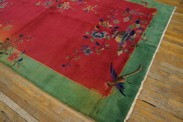 Vivid red rug with a wide green border, featuring detailed multicolored floral designs and exotic birds on wood floor.