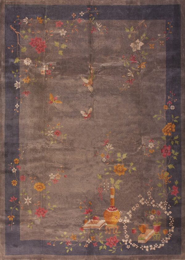 Low-pile rug with a taupe field, indigo border, and multicolored vines, flowers, butterflies, and decorative objects.