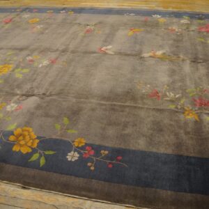Gray low-pile rug with colorful floral and avian motifs, framed by a wide blue border on wood planks.