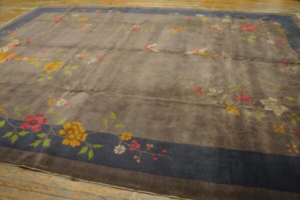 Gray low-pile rug with colorful floral and avian motifs, framed by a wide blue border on wood planks.