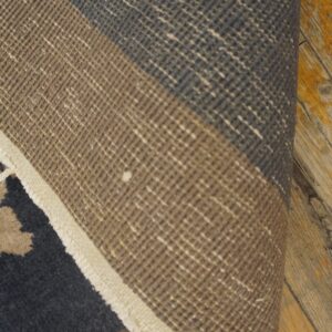 Low-pile rug in brown and dark gray is partially rolled, showing its woven texture on wood planks.