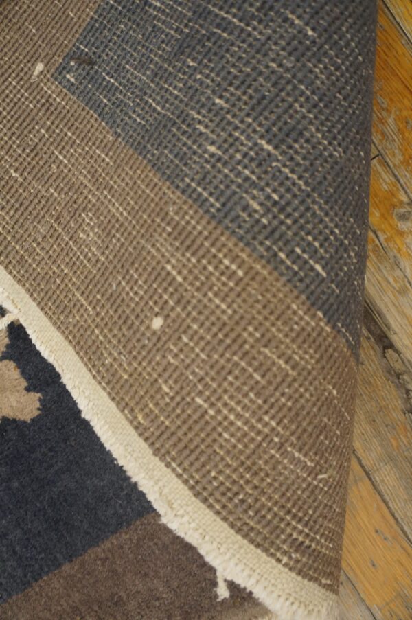 Low-pile rug in brown and dark gray is partially rolled, showing its woven texture on wood planks.
